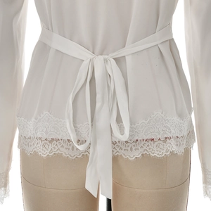 Detail of white long sleeve top featuring waist tie-back and eyelash lace trim hem