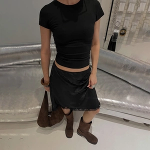Dettaglio del top nero aderente abbinato a gonna in seta con bordo in pizzo