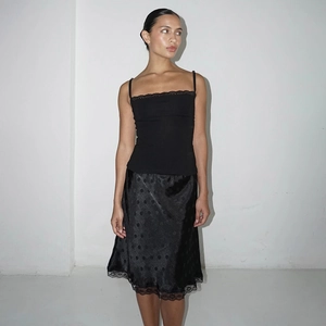 Dettaglio della gonna in raso nero con texture a pois e bordo elegante in pizzo