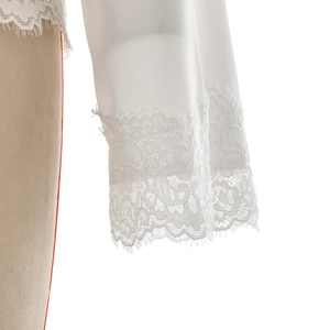 Detailed close-up of exquisite white floral lace hemline on elegant long-sleeve top