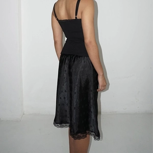 Dettaglio gonna in raso nero con pois sottili ed elegante bordo in pizzo sull'orlo