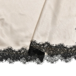 Detail of elegant champagne satin fabric with delicate black eyelash lace trim stitching