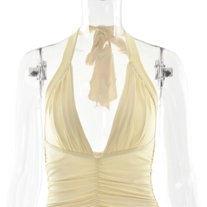 Detail of light yellow halter dress featuring a deep V-neckline and elegant pleats