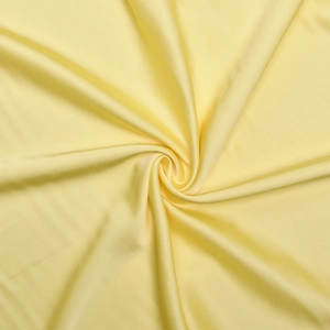 Gros plan sur le tissu satiné jaune pâle soyeux avec plis spiraux et reflets doux