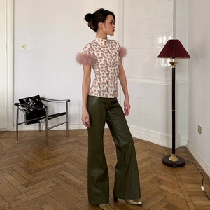 Detail of floral mock neck top featuring plush purple feather cuffs and green faux leather pants