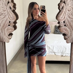 Detail of a one-shoulder striped mini dress with purple and blue diagonal patterns