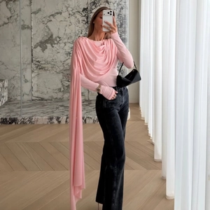 Detail of pink slim-fit long sleeve top featuring asymmetric cascading ruffles and streamers