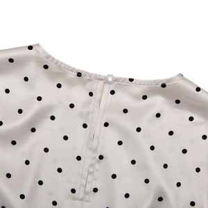 Détail de l'encolure en satin à pois avec un bouton perle délicat sur le dos du col