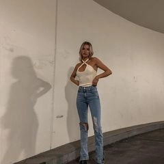 Detail of light beige criss-cross halter neck top paired with ripped blue denim jeans