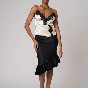 Détail de la jupe mi-longue en satin noir avec ourlet plissé élégant et coupe asymétrique
