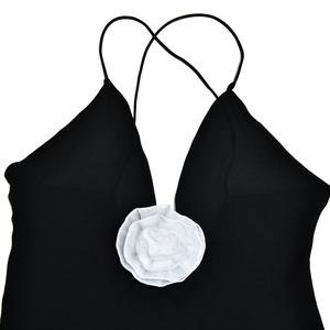 Detail of elegant black V-neck dress featuring a 3D white fabric flower and cross straps