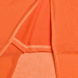 Gros plan du tissu en maille orange avec coutures précises sur l'ourlet et fente latérale