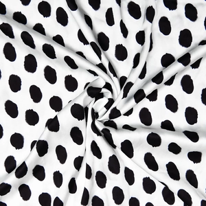 Close-up of smooth satin fabric with large black polka dots and elegant glossy drape