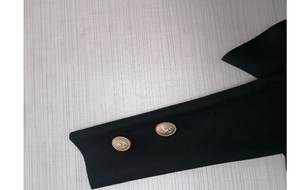 Detail of black knit fabric with luxury lion head gold buttons on the sleeve cuff