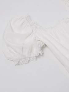 Detail of square neckline with lace trim and pleated puffed sleeves on a white dress