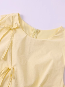 Détail d'une robe sans manches jaune clair avec nœuds latéraux et fermeture éclair dos