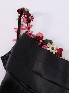 Dettaglio di abito in raso nero con tessuto arricciato e spalline ricamate a fiori colorati