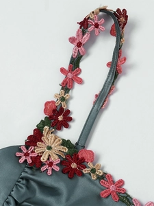 Détail macro de la robe en satin vert foncé avec broderie florale raffinée sur le décolleté