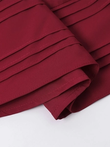 Close-up of dark red pleated fabric detailing with neat double stitching and layered tucks