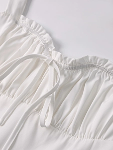 Detail of white summer dress featuring ruffled neckline, drawstring tie, and pleated fabric