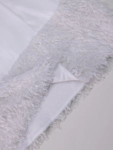 Détail de la robe en satin blanc présentant une bordure en plumes et ourlet à franges