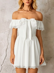 Detail of white off-shoulder mini dress featuring large bow and delicate lace trim