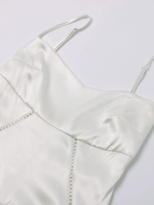 Detail of white matte satin dress showing adjustable spaghetti straps and hollow-out lace