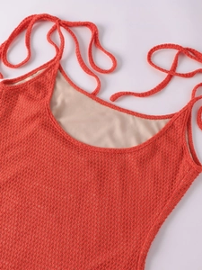 Detail of coral orange knit mesh dress showing shoulder straps and intricate fabric texture