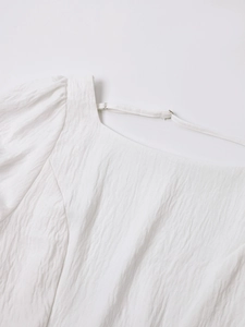 Close-up of square neckline and pleated puff sleeves on white textured vacation dress