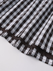 Detail of gingham dress hem featuring brown plaid pattern and fine stitched piping edges