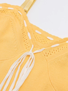 Detail view of yellow knit dress with V-neckline, hollow texture and white braided ties
