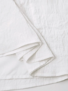 Detailed close-up of white linen fabric texture and fine stitching on the summer dress hem