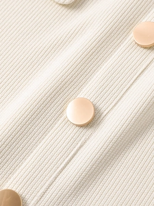 Close-up of cream ribbed knit fabric with elegant gold buttons arranged diagonally