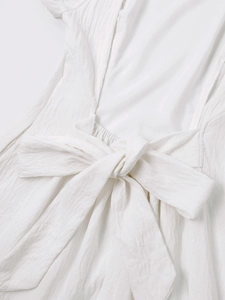 Detail of white crepe summer dress featuring an elegant back bow tie and textured fabric