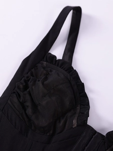 Detail of black mesh corset top with ruffled trim, wide straps, and pleated cup fabric