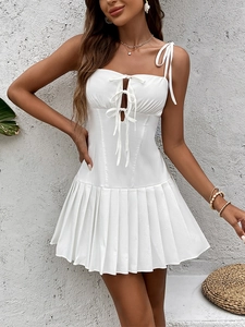 Detail of white mini dress featuring front bow ties, cutout accents and pleated skirt texture