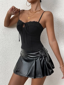 Detail of lace-up bodice top with delicate bow and matching black pleated PU mini skirt