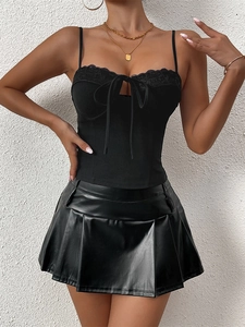 Detailed view of black lace-up crop top with bow and matching faux leather pleated skirt