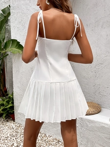Detailed back view of white backless pleated mini dress with tie straps in garden setting
