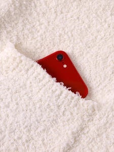 Close-up of soft beige plush fabric with a large functional pocket and phone for scale