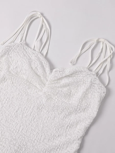 Close-up of white lace dress featuring intricate pleated texture and thin shoulder straps
