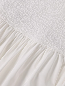 Detail of white dress showing smocking elastic texture and flowing pleated fabric