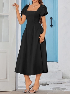 Close-up of a black A-line dress with square neck and puff sleeves against a blue wall