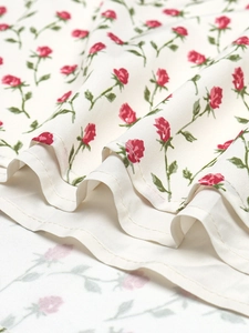 Détail de l'ourlet de la robe avec imprimé rose rouge et coutures fines sur tissu crème