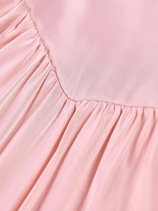 Detailed close-up of pink satin fabric showing fine pleats and neat stitching on the dress