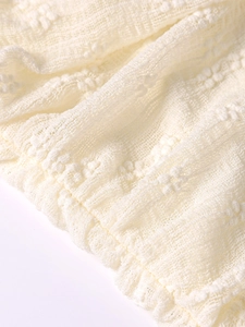 Macro detail of cream pointelle fabric featuring delicate ruffles and knit texture