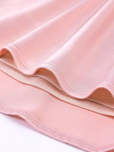 Detail of light pink satin dress hem featuring smooth pleated fabric and premium double stitching