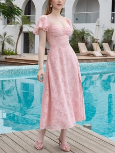 Détail du tissu jacquard fleuri rose sur une robe à décolleté en cœur et volants