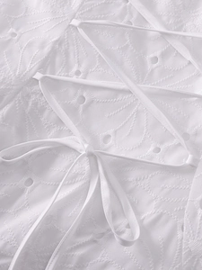 Close-up of white jacquard fabric featuring hollow embroidery and criss-cross tie details