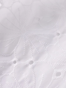 Detailed macro view of white floral jacquard fabric with intricate embroidery and eyelets